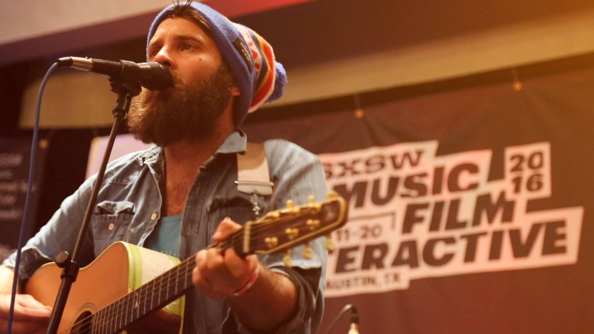 guitarist performs live music at a microphone with a sign behind him that reads: SXSW 2016 Music Film Interactive